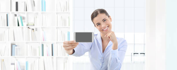 istock smiling woman showing smartphone in her hand on interior office background 840646776