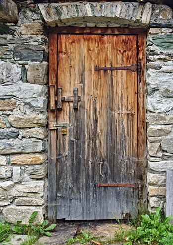 Old wooden door in field stone wall with big rusty hinges and padlock