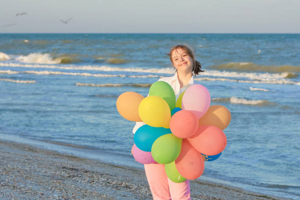 Happy Girl seventeen-year-old with Down syndrome on the beach with balloons. Positive human emotions, feelings.