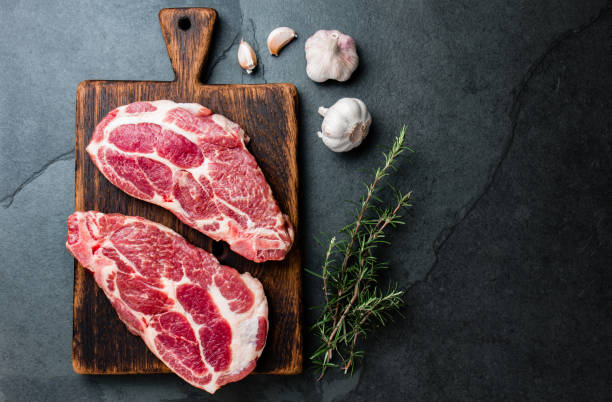 Raw pork cutlet chop for grill BBQ with herbs on wooden board, slate background, top view, copy spaces stock photo