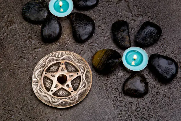 Photo of Turquoise candles with black rocks and silver pentagram on gray slate background with water droplets