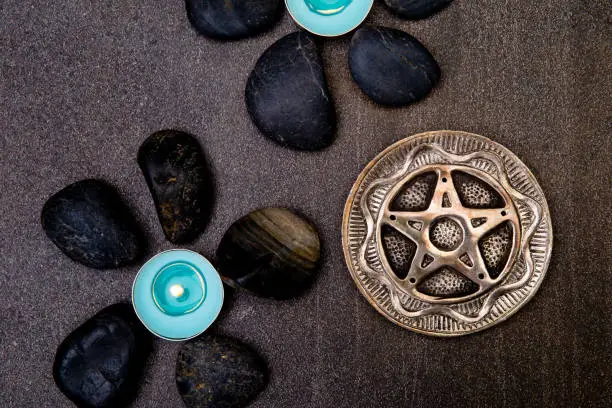 Photo of Turquoise candles with black rocks and silver pentagram on gray slate background