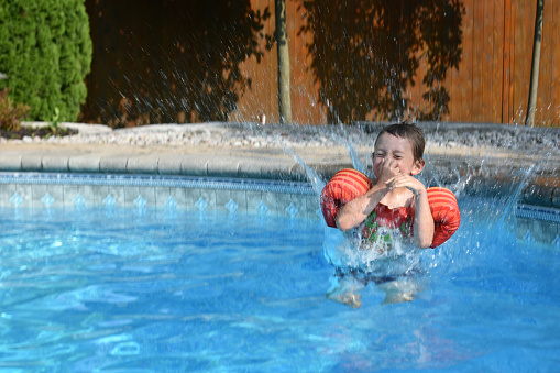 A boy in the pool after jumping in causing a big splash