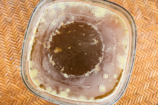 Refrigerated gellatinous lamb bone broth with a thin layer of fat in a glass bowl