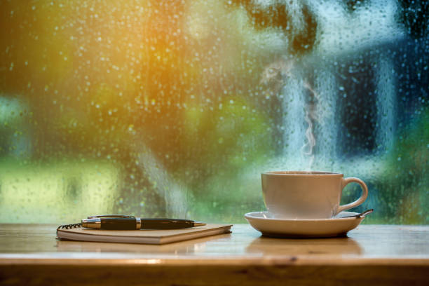 Cup of coffee, notebook and pen on wooden table on rainy day. stock photo