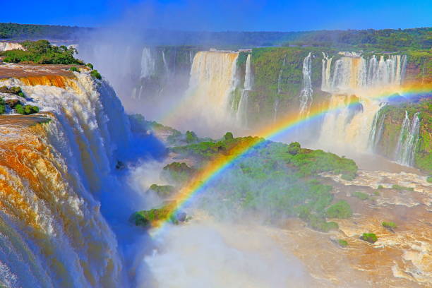 Impressive Iguacu falls with rainbow, one of the most beautiful waterfalls in the world and one of the seven Wonders of Nature, dramatic beauty in nature landscape - Idyllic Devil's Throat - international border of Brazilian Foz do Iguacu city, Parana State, Argentina Puerto Iguazu city, Misiones province and Paraguay - rainforest landscape panorama, South America