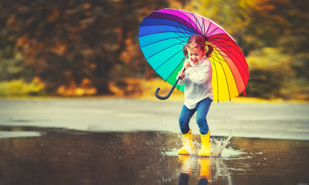 fille enfant drôle heureux avec parapluie, sauter sur les flaques d’eau dans les bottes en caoutchouc - colors color image rainbow umbrella photos et images de collection