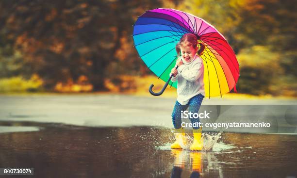 Happy Funny Child Girl With Umbrella Jumping On Puddles In Rubber Boots Stock Photo - Download Image Now