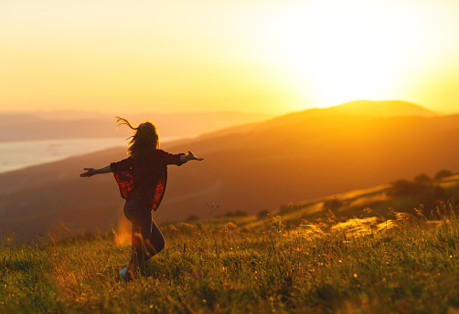 Happy woman with open hands dances,  rejoices, laughs  on sunset in nature