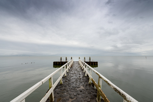 view from jetty on a calm sea, clouds reflect in the water