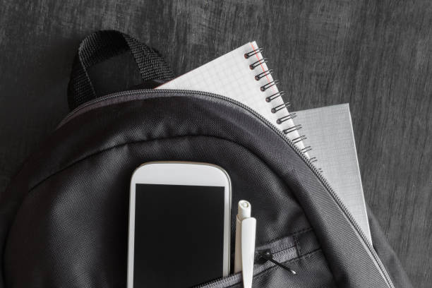 istock Smart phone, notes and pen in the student bag on the black wooden table. Education concept. Ready for new school year. Empty place for a text on the mobile phone. 840745982