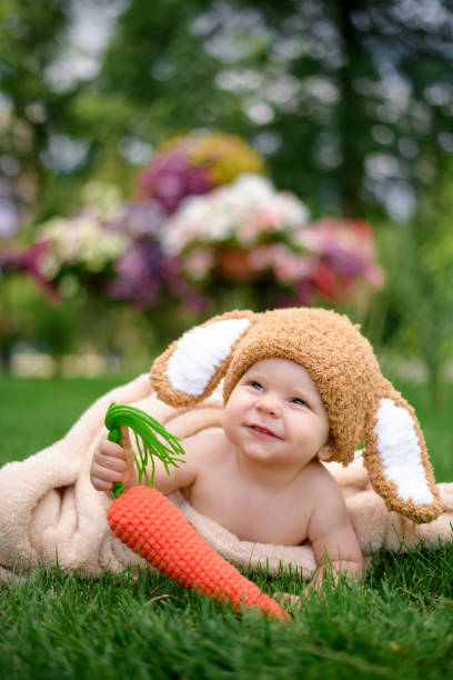 baby in the hat like a bunny with carrot toy on green grass outdoors - ravena imagens e fotografias de stock