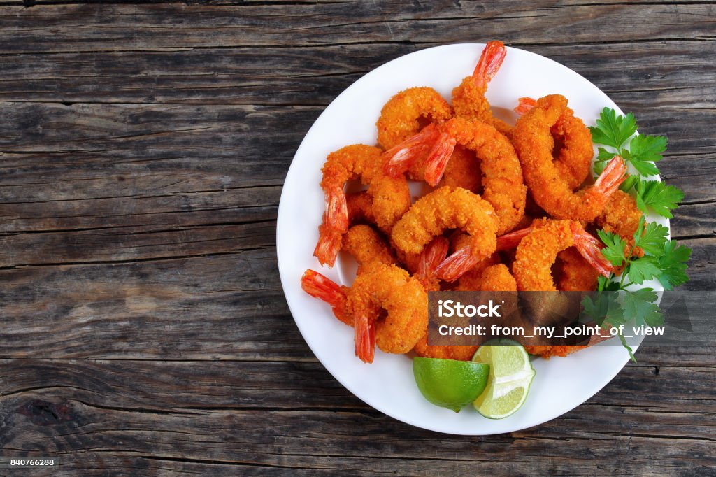 tasty breaded shrimps on white plate delicious deep fried breaded shrimps served with lime wedges and coriander leaves on white plate on wooden table, copy space for text, view from above Shrimp - Seafood Stock Photo