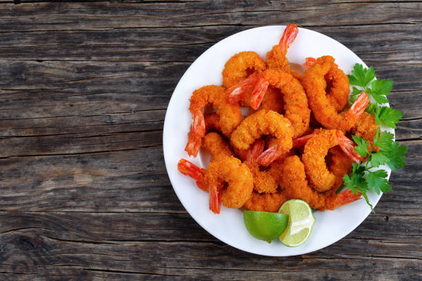 tasty breaded shrimps on white plate delicious deep fried breaded shrimps served with lime wedges and coriander leaves on white plate on wooden table, copy space for text, view from above breaded photos stock pictures, royalty-free photos & images