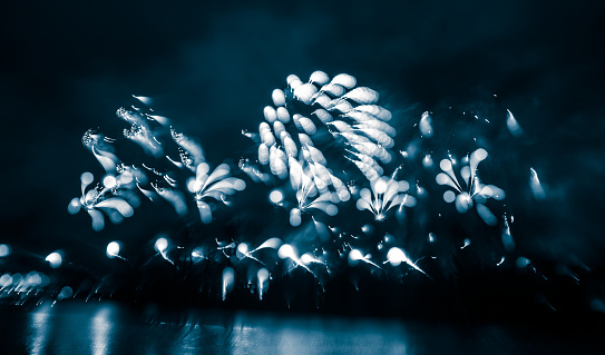 Abstract, blurry, bokeh-style colorful photo of fireworks in a blue tone above the river