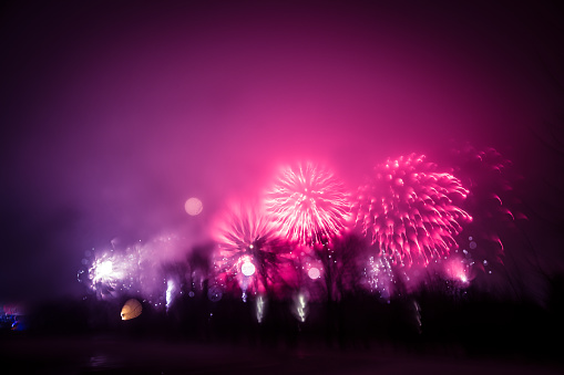 Abstract, blurry, bokeh-style colorful photo of fireworks in a purple tone above the river