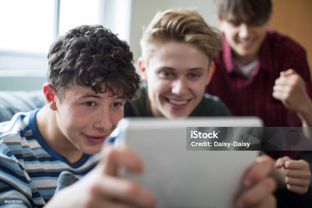 Three Teenage Boys Playing Game On Digital Tablet At Home Domestic Life Stock Photo
