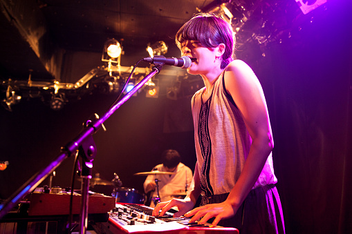 A young Japanese woman is playing an electronic keyboard while singing at a live event.