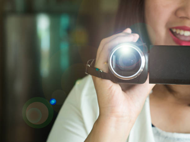 happy smiling woman with hand holding video camera or camcorder recording some happy events coming in her life with beautiful lens flare - camera lens home video camera broadcasting imagens e fotografias de stock