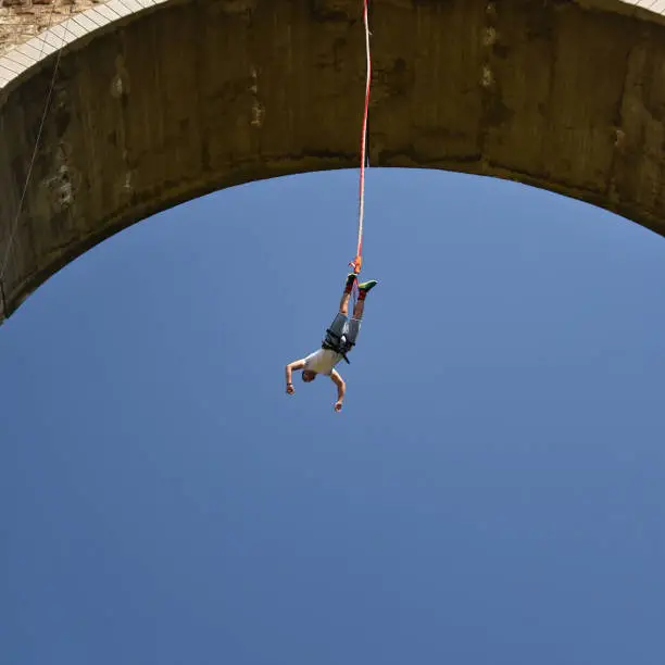 Young man bungee jumper hanging on a cord, sunny summer day with blue sky, Bunovo, Bulgaria