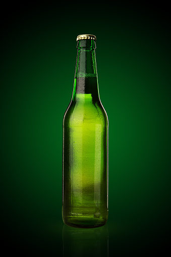 Cold wet beer bottle on green background