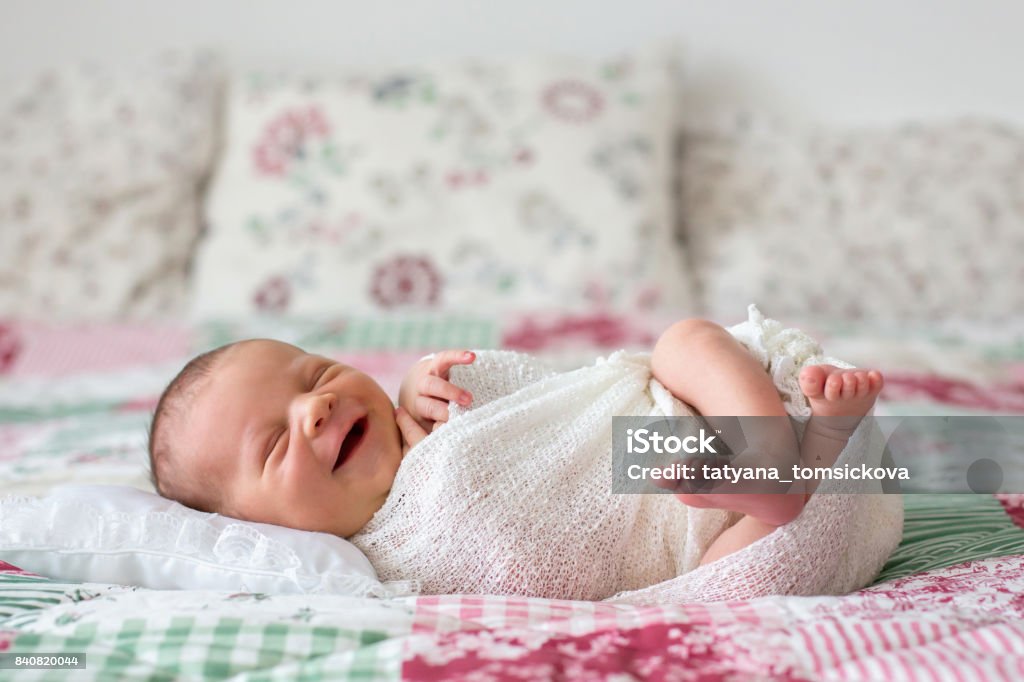 Garçon beau bébé nouveau-né, souriant largement, enveloppé dans une pellicule, couchée dans son lit - Photo de Sourire libre de droits