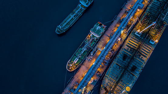 Aerial view Crude oil tanker under cargo operations on typical shore station with clearly visible mechanical loading arms and pipeline infrastructure.