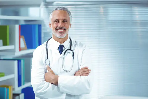 Portrait of doctor smiling and standing with arms crossed at clinic