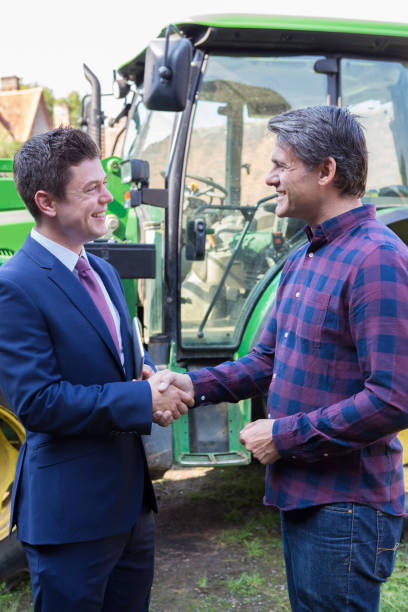農家とバック グラウンドでトラクターと握手するビジネスマン - tractor farm uk agriculture ストックフォトと画像