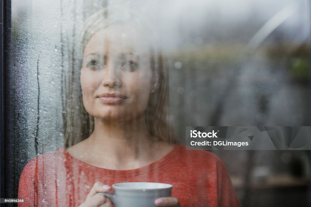 I'm Glad I'm Not Out In The Rain Woman is drinking a cup of tea while looking out of a window in her home. Rain Stock Photo