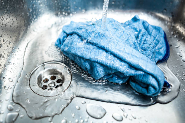 blaue mikrofasertuch unter fließendem wasser in der spüle - kitchen cloth stock-fotos und bilder