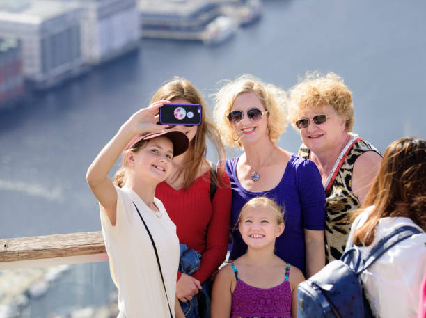 Family enjoying the view from top of Mount Fløyen. Bergen city Bergen, Norway - August 9, 2017: Family enjoying the view from top of Mount Fløyen taking selfie. Bergen city including seen in background. Cruising ships in port. fløyen stock pictures, royalty-free photos & images