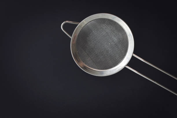 Black hand strainer isolated over a yellow background.