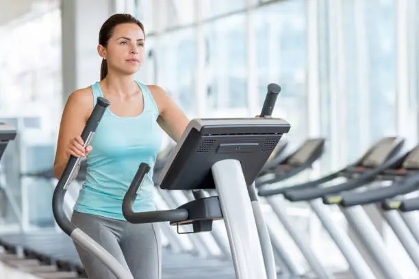 Beautiful Latin American woman exercising at the gym on a cross trainer - healthy lifestyle concepts