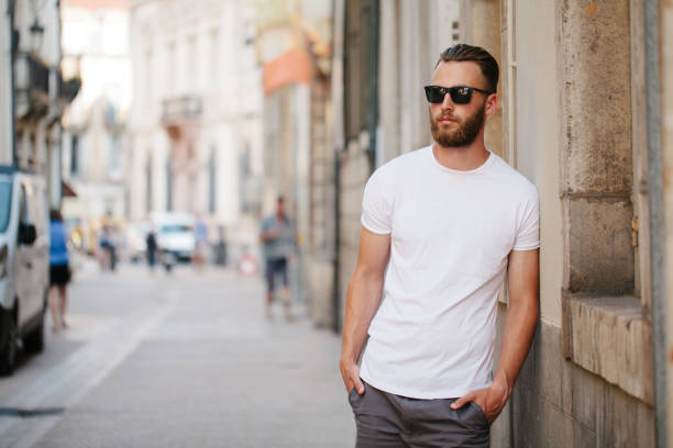 Hipster handsome male model with beard wearing white blank t-shirt with space for your logo or design in casual urban style Hipster handsome male model with beard wearing white blank t-shirt with space for your logo or design in casual urban style alternative pose photos stock pictures, royalty-free photos & images