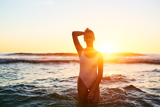Shot of a young woman standing in the water at sunset