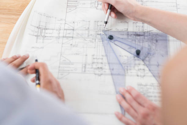 Two sets of hands measure and draw on a blueprint