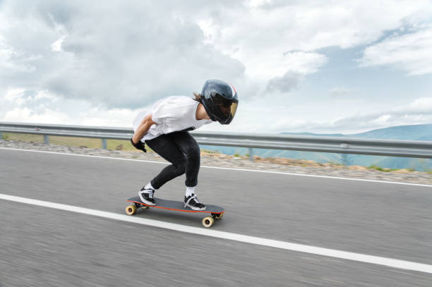 un chico en un casco integral es montado en una carretera a gran velocidad en la lluvia - patinaje en tabla larga fotografías e imágenes de stock