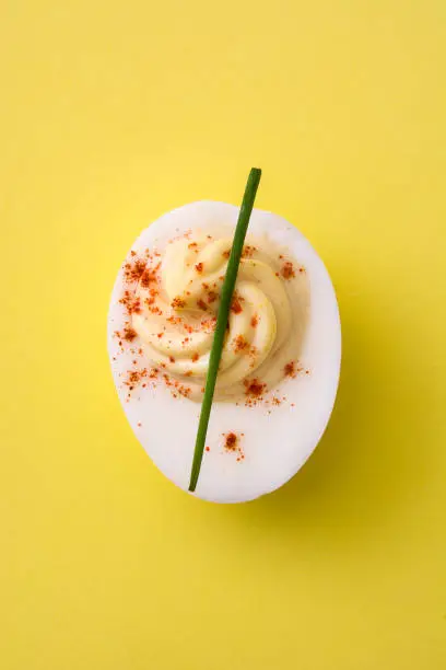 Classic stuffed egg with paprika on yellow background