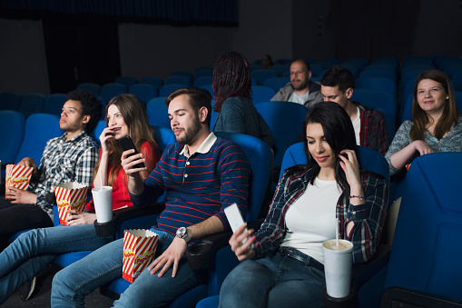 Young adults at the cinema watching movie and some of them using their cell phones