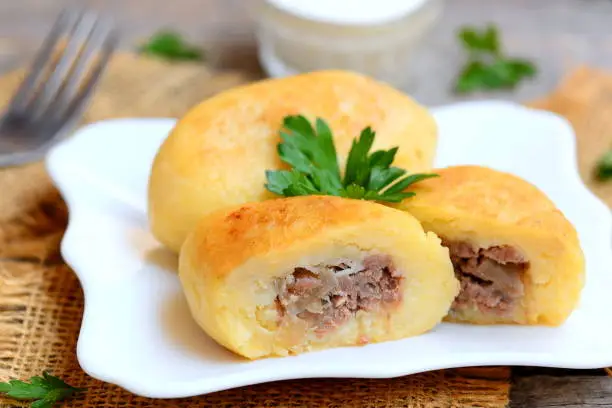 Photo of Potato zrazy with a meat filling on a white plate and a vintage wooden table. Traditional Ukrainian zrazy recipe. Closeup