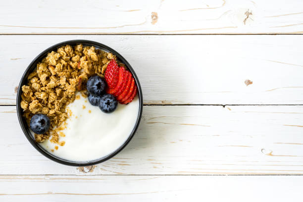 tigela de granola com iogurte, frutas frescas, morango na mesa de madeira. - granola breakfast dieting food - fotografias e filmes do acervo