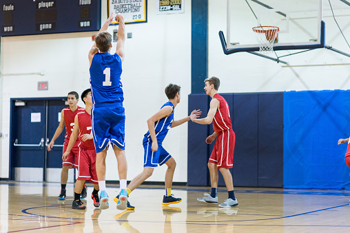 Boys high school basketball team: player shoots a three-pointer over opponent