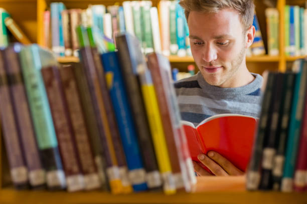 istock Student reading a book amid bookshelves in the library 840968372
