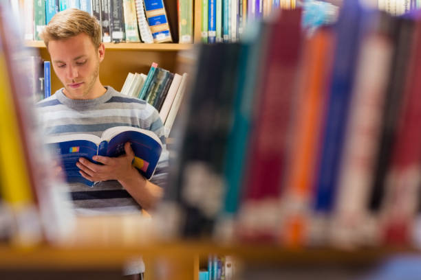 istock Male student reading a book in the library 840968482