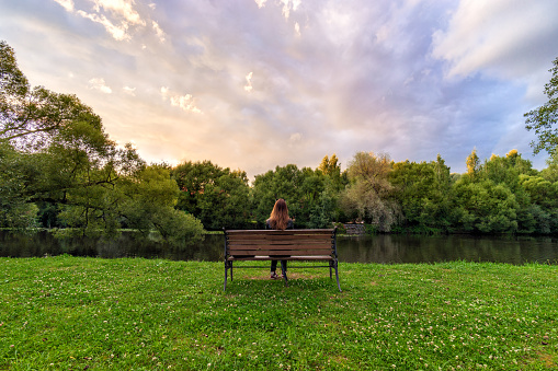 A Young Woman Sitting Alone On A Bench In Green Park And Looking On Nature