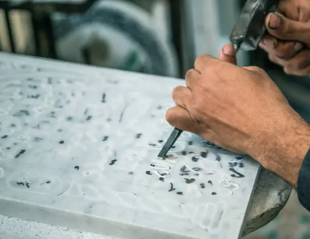 Carving out Arabic letters of marble headstone with a chisel