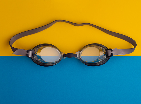 top view of swimming goggles on blue and yellow background paper
