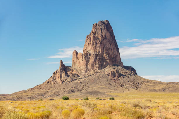 El Capitan or Agathla Peak rises over 1500 feet (457 meter) above the surrounding terrain. It's an eroded volcanic plug. Beautiful view under blue summer sky with fluffy cloudscape. South Monument Valley, Navajo Volcanic Field, Arizona, USA