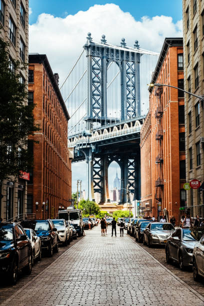 Tourists standing in the middle of the road at Washington Street, Brooklyn looking at the classic view of the east tower of Manhattan Bridge, New York City, USA. The Empire State Building is framed within the lower arch of the bridge.